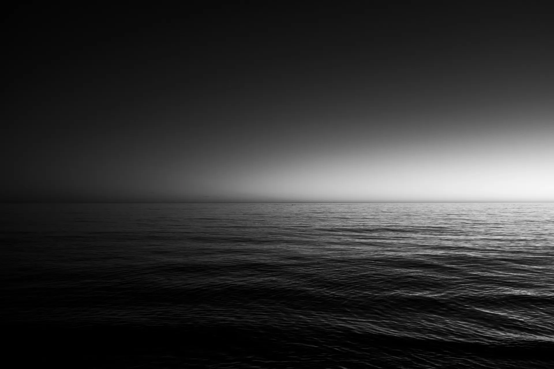 Mar en calma en blanco y negro, con la luz del horizonte al fondo